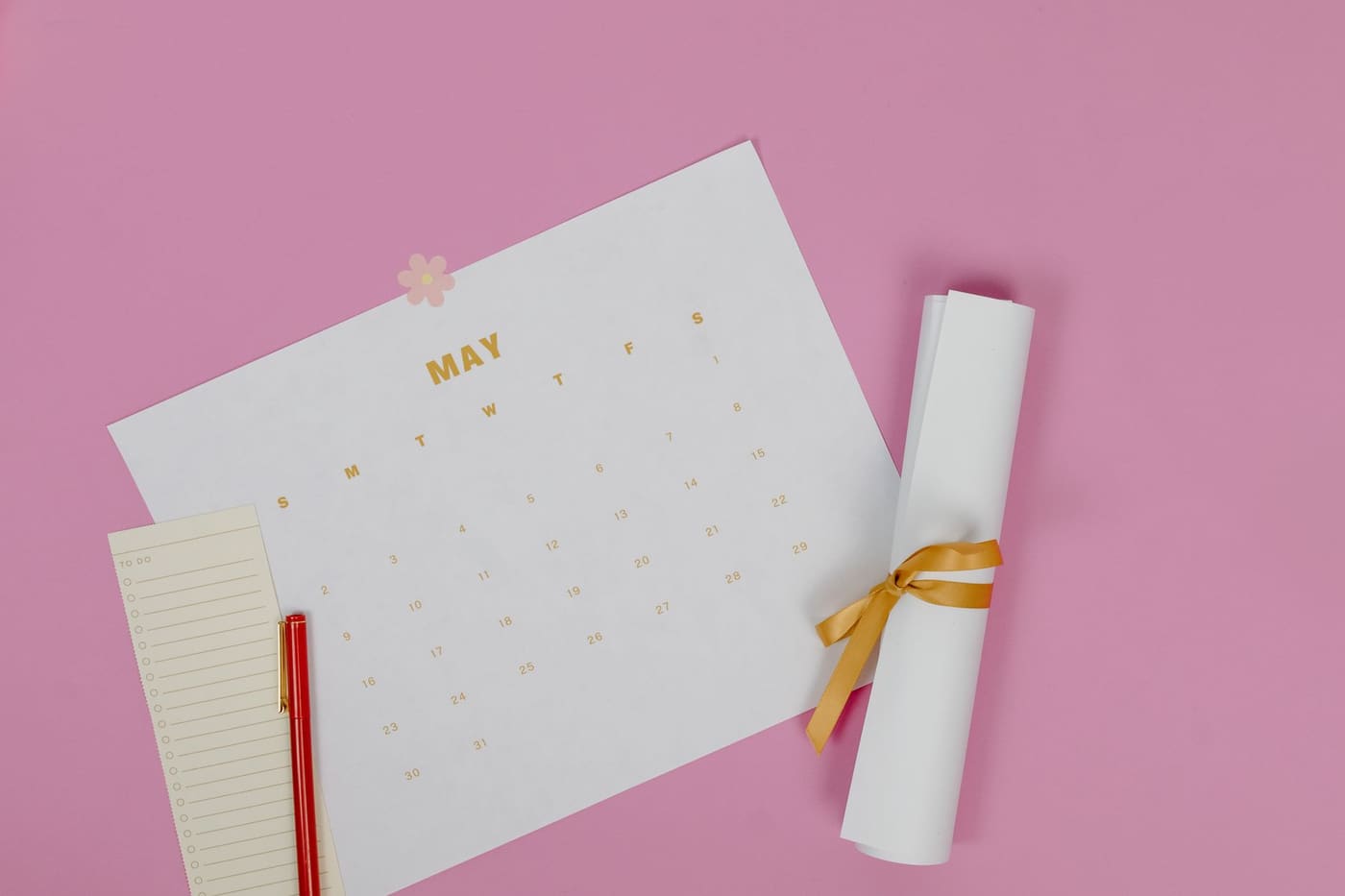 A May calendar page with a pen and a rolled paper on a pink background